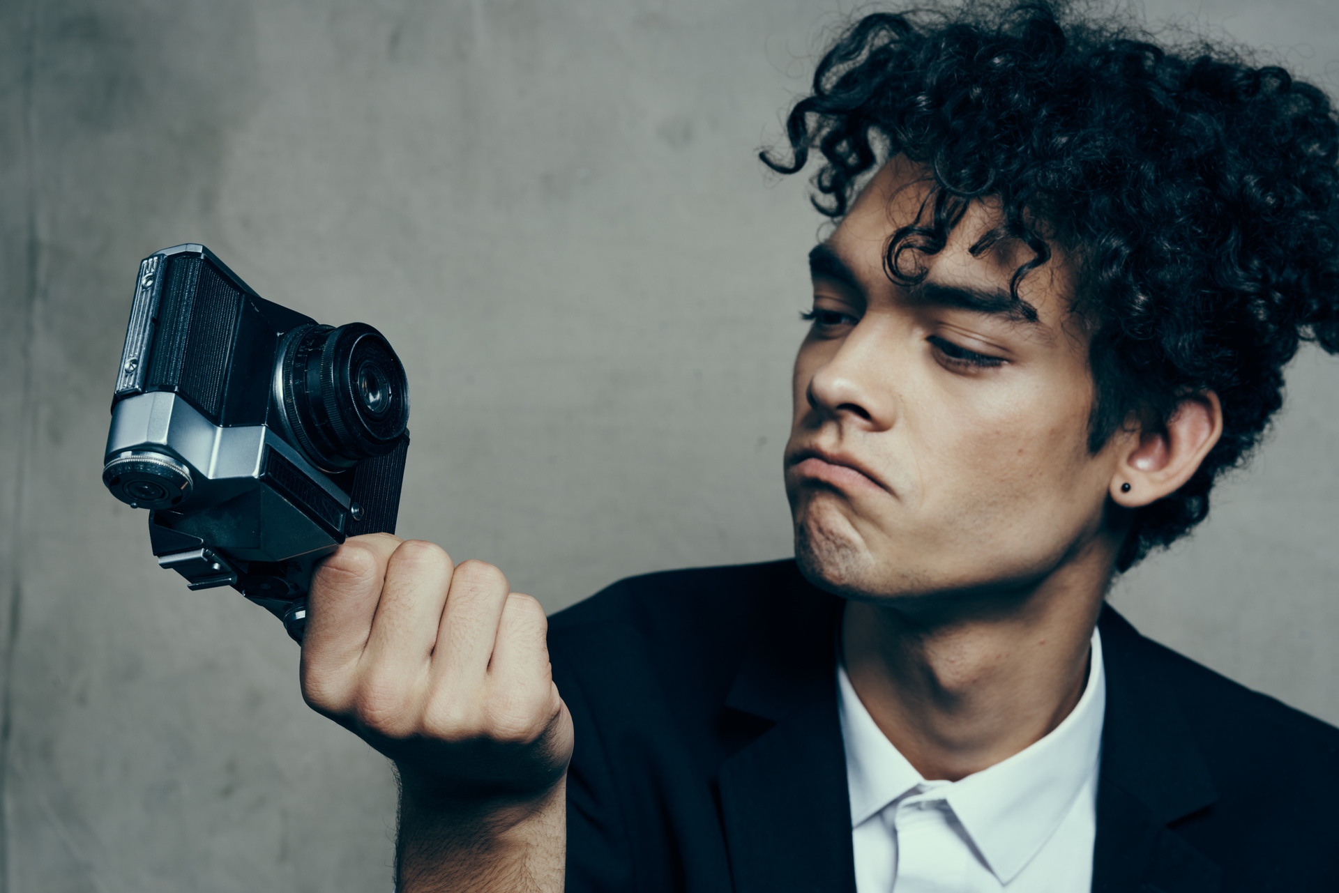 Stylowo ubrany młody mężczyzna z kręconymi włosami i z aparatem w ręku w studio fotograficznym