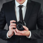 Mężczyzna w garniturze trzyma czarną cyfrowy aparat do robienia zdjęć portretowych