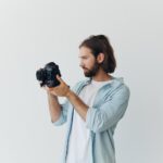 Fotograf w studiu na białym tle patrzy przez wizjer aparatu i robi zdjęcia 360 wysokiej jakości