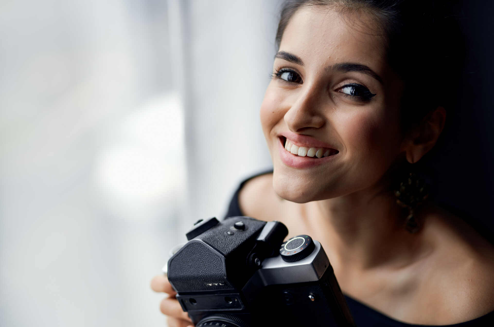 Młoda kobieta trzyma aparat w ręku. Zajmuje się fotografią portretową